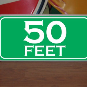 May include: Green sign with white lettering that reads "50 FEET".