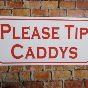 May include: A rectangular white sign with rounded corners and a thin red border. The text PLEASE TIP CADDYS is printed in bold, red, capital letters in the center of the sign. The sign has a flat, smooth surface and a clean finish.
