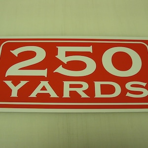 May include: A red rectangular sign with white text that reads "250 YARDS".