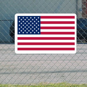 Può includere: Un cartello rettangolare bianco con una bandiera americana rossa, bianca e blu stampata su di esso. La bandiera è centrata sul cartello ed è circondata da un bordo bianco.