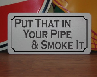 以下が含まれることがあります： 「Put that in your pipe & smoke it」と書かれた白い金属製の看板です。