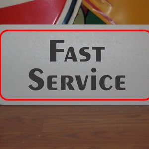 Puede incluir: Un letrero blanco con borde rojo, el texto "FAST SERVICE" en letras negras.