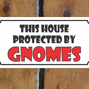 Puede incluir: Un cartel blanco con borde negro y esquinas redondeadas. El cartel dice "This house protected by gnomes" en texto negro. La palabra "gnomes" está en texto rojo.