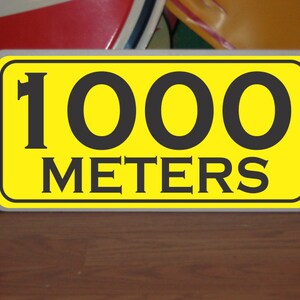 May include: A yellow sign with black text that reads "1000 METERS".