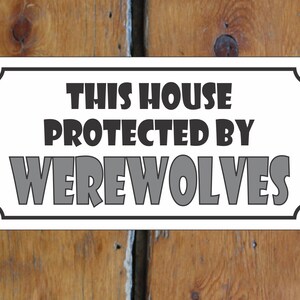 Puede incluir: Señal blanca con borde negro y esquinas redondeadas. La señal dice "Esta casa protegida por hombres lobo".