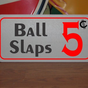 May include: A white sign with a red border and black text that reads "Ball Slaps 5¢". The number 5 is red and the cent symbol is black.