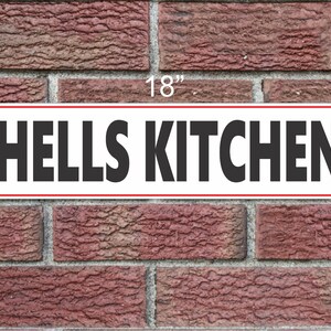 May include: A white rectangular sign with a red border, reading "HELLS KITCHEN" in black bold letters. The sign is 18 inches wide and 6 inches tall.