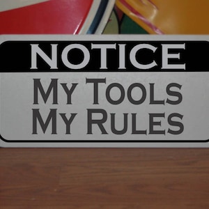Puede incluir: Un letrero de metal plateado con letras negras que dice "NOTICE MY TOOLS MY RULES".
