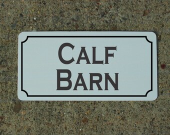 May include: White rectangular sign with black border and rounded corners. The sign says "CALF BARN" in black serif font.