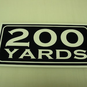 May include: A black and white sign with the number 200 and the word "YARDS" in white lettering.