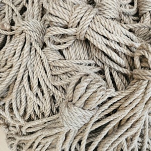 May include: Close-up of a pile of thick, beige-coloured rope. The rope is tightly wound and knotted in several places, creating a textured and natural appearance. The image highlights the rope's coarse texture and neutral colour.