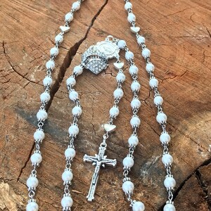 May include: White pearl rosary with a silver crucifix and a silver charm with the word "QUINCEA&Ntilde;ERA" and rhinestones.