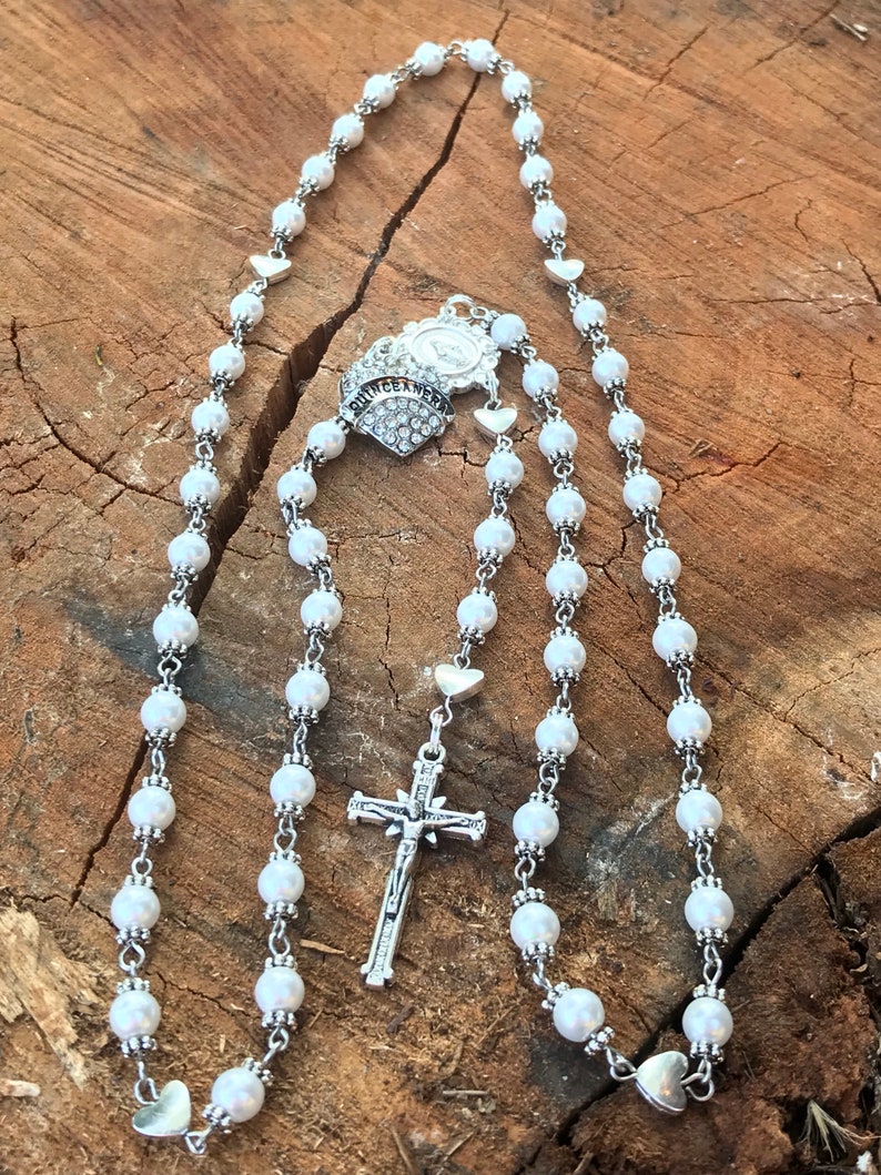 May include: White pearl rosary with a silver crucifix and a silver charm with the word "QUINCEA&Ntilde;ERA" and rhinestones.