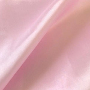 May include: A smooth, pale pink fabric with a subtle sheen. The fabric is folded in half, creating a soft, flowing drape.