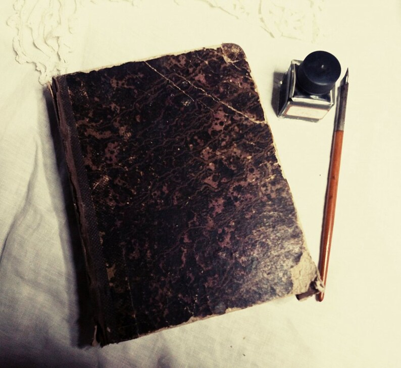 May include: A vintage, dark brown leather-bound journal with a worn and textured cover. A black inkwell and a quill pen are placed on a white surface next to the journal.