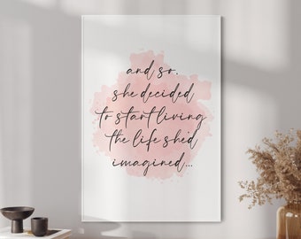 Puede incluir: Un cuadro enmarcado con la cita "and so, she decided to start living the life she imagined..." en escritura negra sobre un fondo rosa acuarela. El cuadro se exhibe sobre una superficie de madera con objetos decorativos.