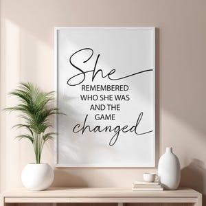 May include: A white framed print with black text that reads "She remembered who she was and the game changed".