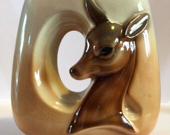 May include: A ceramic vase with a brown and white glaze. The vase has a cutout in the shape of a deer's head. The deer's head is brown with a white background.