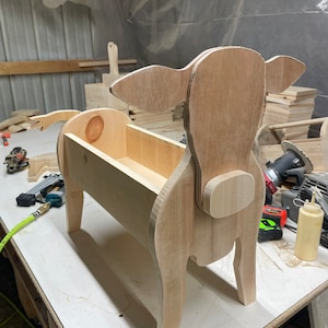 May include: A wooden cow planter with a rectangular planter box. The cow is made of unfinished wood and has a light brown color.