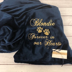 May include: A navy blue fleece throw blanket with gold embroidery that reads "Blondie Forever in our Hearts" with three gold paw prints.
