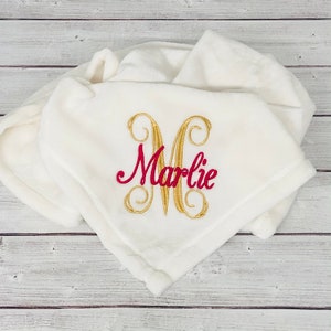 May include: White plush blanket with a gold embroidered letter M and the name "Marlie" in red embroidery.