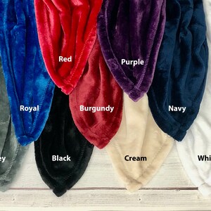 May include: A variety of plush blankets in different colors, including grey, royal blue, red, burgundy, purple, navy, cream, and white. The blankets are arranged in a row, with the colors alternating.