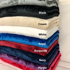 May include: A stack of ten plush blankets in various colors, including grey, black, cream, white, royal blue, burgundy, navy, purple, and red. Each blanket is folded and stacked on top of the other, with the color name written below each blanket.