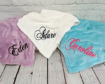 May include: Three soft plush blankets in lavender, white, and turquoise. The lavender blanket features the name Eden in black script, the white blanket features the name Adare in black script, and the turquoise blanket features the name Caroline in pink script.