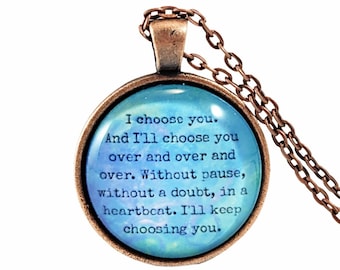 May include: A copper necklace with a round glass pendant featuring a blue and white watercolor background with a quote that reads: "I choose you. And I'll choose you over and over and over. Without pause, without a doubt, in a heartbeat. I'll keep choosing you."