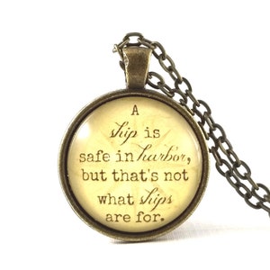 May include: A bronze necklace with a round glass pendant featuring a quote about ships and harbors: "A ship is safe in harbor, but that's not what ships are for."