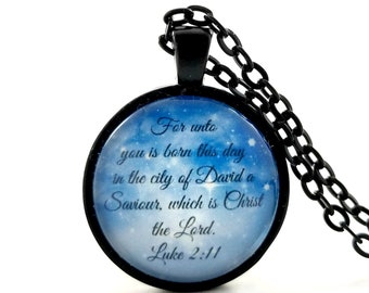 May include: A black chain necklace with a round pendant featuring a blue and white starry sky background with the text "For unto you is born this day in the city of David a Saviour, which is Christ the Lord. Luke 2:11"
