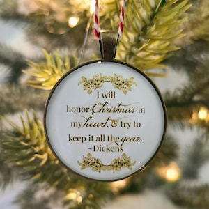 Pu&ograve; includere: Un ornamento rotondo color bronzo con sfondo bianco e testo dorato che recita: I will honor Christmas in my heart, & try to keep it all the year. ~Dickens. L'ornamento &egrave; appeso tramite un cordino ritorto di colore rosso e bianco.