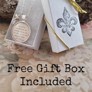 Puede incluir: Un collar con colgante plateado con una cita de C.S. Lewis dentro de un colgante redondo, presentado en una caja de regalo blanca abierta. La caja est&aacute; decorada con un dise&ntilde;o de flor de lis y una cinta dorada. El texto "Free Gift Box Included" tambi&eacute;n es visible.