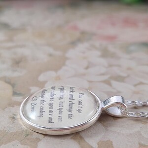 Puede incluir: Un collar con colgante plateado con un dije redondo de cristal transparente. El dije presenta una cita de C.S. Lewis: "No puedes volver atr&aacute;s y cambiar el principio, pero puedes empezar donde est&aacute;s y cambiar el final."
