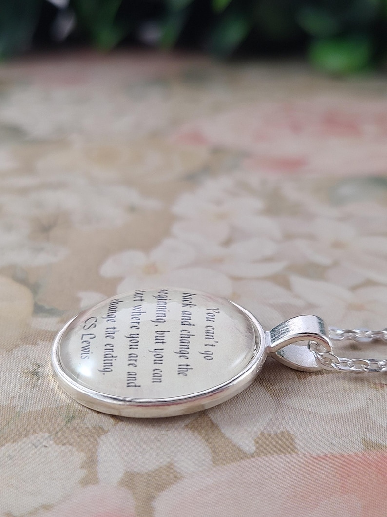 Puede incluir: Un collar con colgante plateado con un dije redondo de cristal transparente. El dije presenta una cita de C.S. Lewis: "No puedes volver atr&aacute;s y cambiar el principio, pero puedes empezar donde est&aacute;s y cambiar el final."