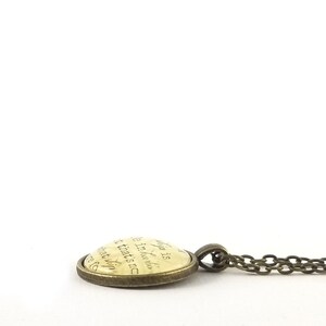 May include: A bronze necklace with a round pendant featuring a cream-colored background with a quote in black script. The quote reads: "Life is a journey, not a destination.  That's what makes it fun."
