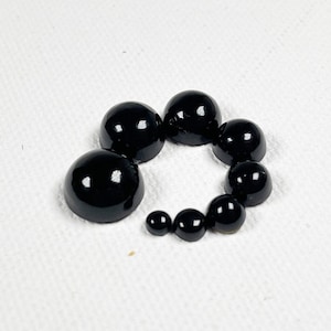 May include: A set of black plastic dome-shaped buttons of varying sizes arranged in a circle.