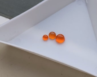 May include: Four orange glass beads of varying sizes on a white triangular tray.