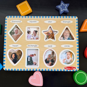 May include: A wooden shape sorting puzzle board featuring eight cutouts labeled diamond, square, star, triangle, heart, rectangle, oval, and circle. Each cutout contains a photograph. Loose wooden shapes in various colors surround the board.