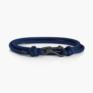 Pode incluir: Um bracelete de corda azul escuro com um fecho de metal preto. O bracelete é feito de uma corda grossa e resistente e tem um design simples e elegante.