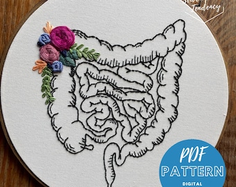 Pode incluir: Um desenho de linha preto e branco do sistema digestivo humano com um design de bordado floral em rosa, azul, verde e laranja. O bordado está no lado esquerdo da imagem. O texto "PDF PATTERN DIGITAL DOWNLOAD" está em azul sobre um círculo branco no canto inferior direito da imagem.