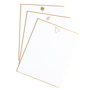 Pode incluir: Três cartões de correspondência brancos com bordas douradas e um design dourado em cada cartão. Os designs incluem um trevo de quatro folhas, uma joaninha e uma ferradura.