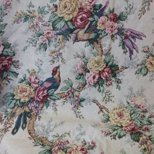 May include: A beige fabric with a floral pattern featuring pink, yellow, and red roses and blue birds. The fabric has a vintage aesthetic.