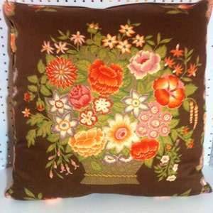 May include: A brown pillow with a floral design. The flowers are in a basket and are in shades of orange, pink, and white.