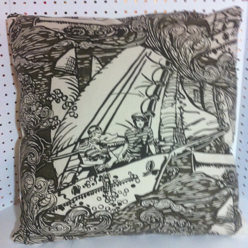 May include: A cream-colored pillow with a black and white illustration of a sailboat with two people on board. The sailboat is sailing through a stormy sea with waves crashing around it. The background is a dark gray color.