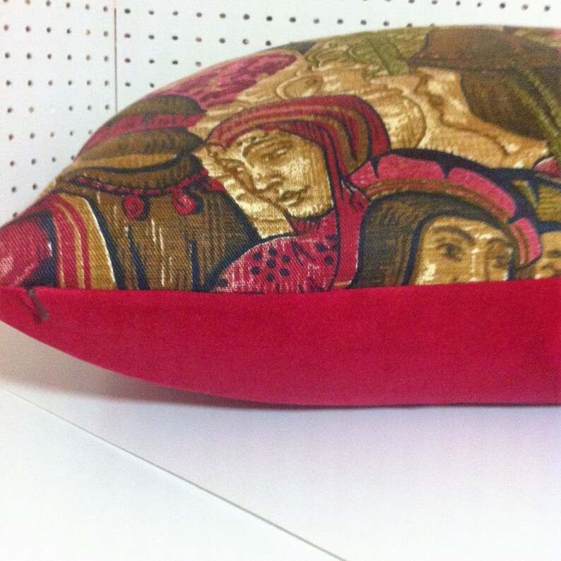 May include: A red and gold patterned pillow with a red velvet border. The pattern features a group of people in medieval clothing.