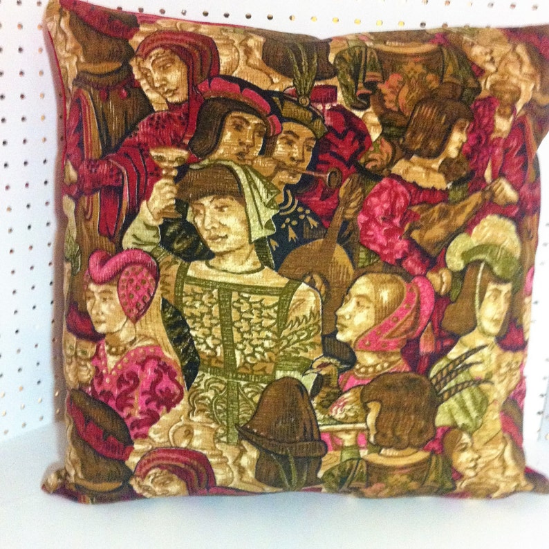 May include: A decorative pillow with a medieval tapestry design featuring people in colorful clothing and a musical instrument. The background is a rich brown with gold accents.