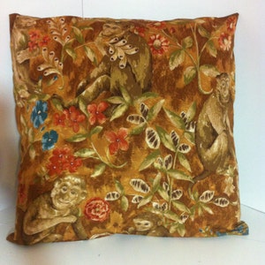 May include: A brown throw pillow with a repeating pattern of monkeys and leafy vines. The monkeys are brown and have a light brown face. The vines are green and have brown leaves.