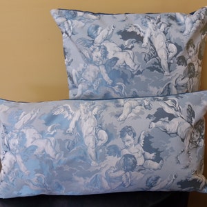 May include: Two decorative throw pillows with a blue and white pattern of cherubs and clouds. The pillows have a dark blue trim.