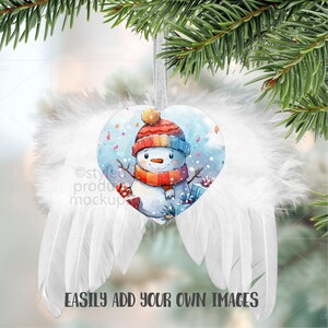 May include: A heart-shaped Christmas ornament featuring a watercolor snowman wearing a red and blue hat and scarf. The ornament is surrounded by white feather wings and hangs from a silver ribbon. The text "EASILY ADD YOUR OWN IMAGES" is at the bottom.